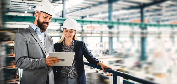 two executives with helmets checking a tablet in an industrial plant